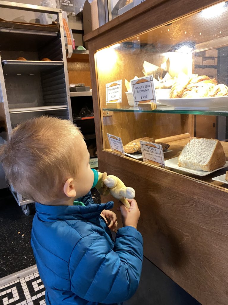 A little boy looking at a case of pastries with a pacifier in his mouth